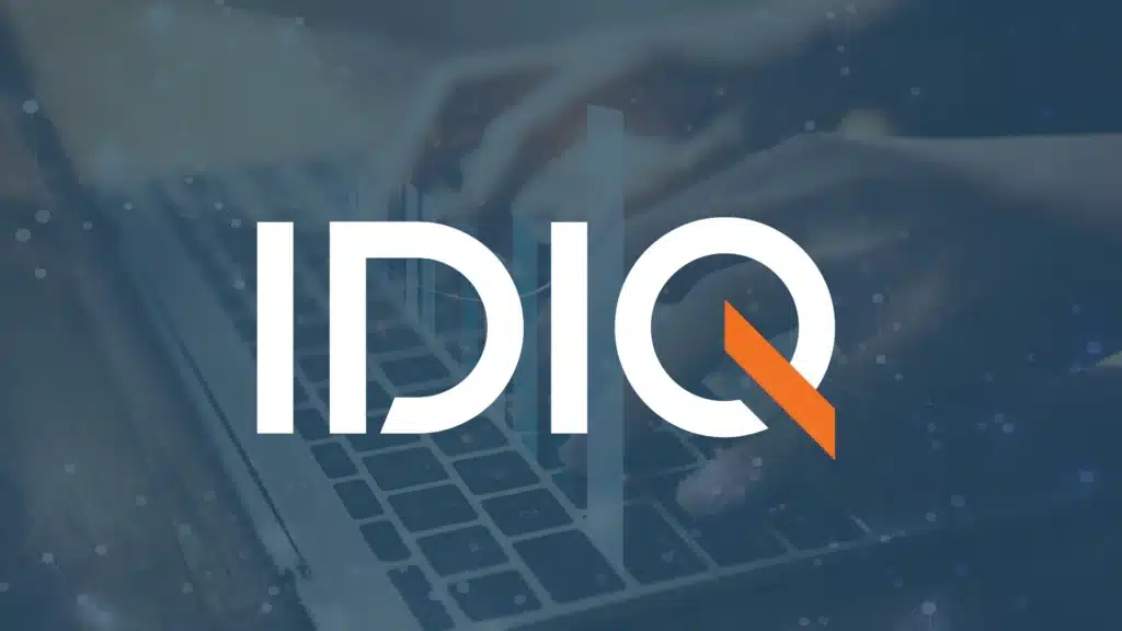 The image features the logo "IDIQ" in large, white text with an orange accent on the "Q." In the background, there is a blurred image of hands typing on a laptop keyboard with a subtle overlay of connected network lines and dots.